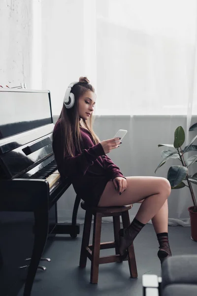 Gadis Headphone Duduk Dan Menggunakan Smartphone Ruang Tamu Dengan Piano — Stok Foto