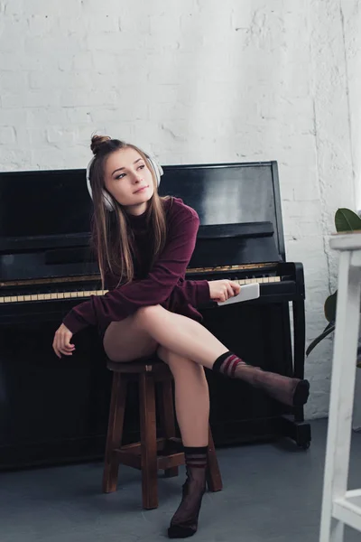 Красива Дівчина Навушниками Голові Сидячи Стільці Перед Піаніно Тримаючи Смартфон — стокове фото