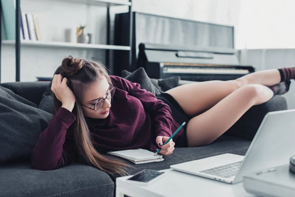 Hermosa Chica Gafas Tumbado Sofá Escritura Cuaderno Con Lápiz Casa —  Fotos de Stock