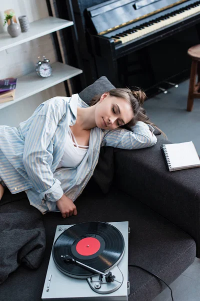 attractive girl sleeping on sofa near vintage record player at home