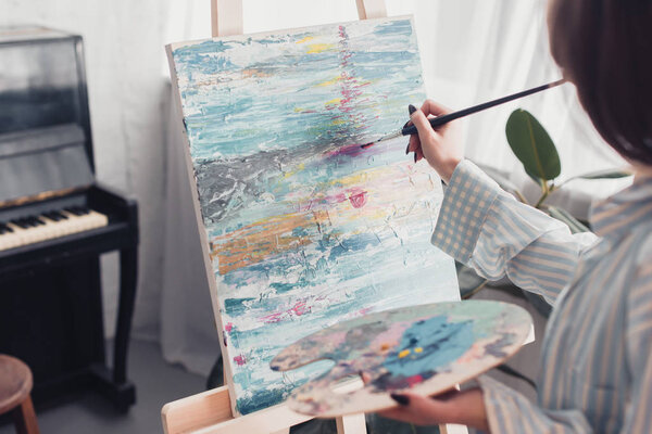 artist holding palette and painting on canvas at home
