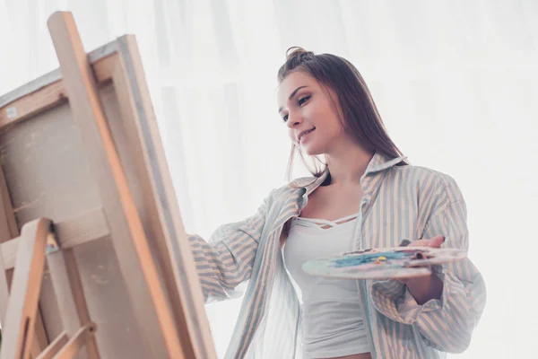 Attraente Artista Tenendo Tavolozza Guardando Cavalletto Soggiorno — Foto Stock