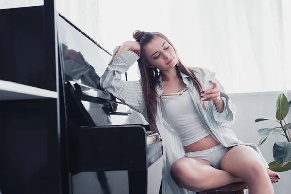 シャツと下着ピアノに座っていると スマート フォンを使用して自宅でセクシーな女の子 — ストック写真