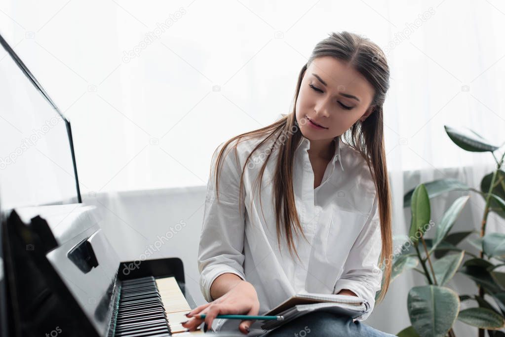 beautiful girl with notebook playing piano and composing music at home