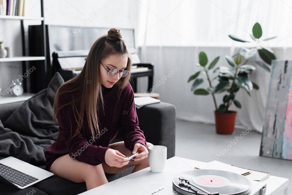 girl sitting at table and rolling marijuana joint in living room