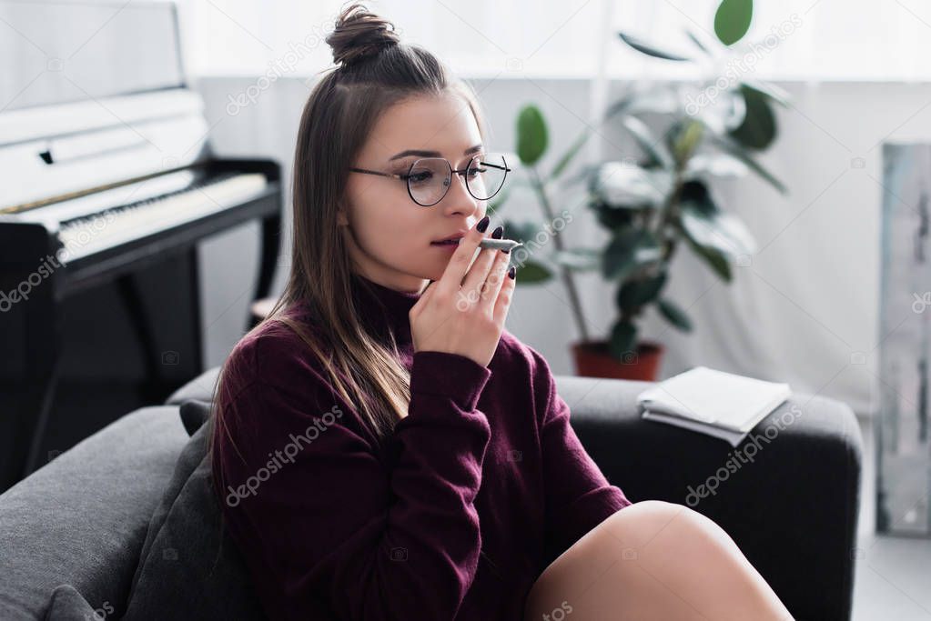 beautiful girl sitting on couch and smoking marijuana joint in living room