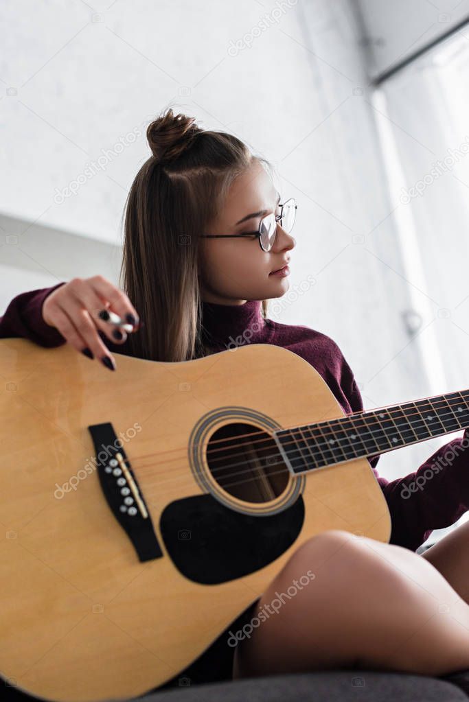 beautiful girl sitting, holding marijuana joint and playing guitar at home
