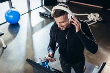 yakışıklı sporcu treadmill egzersiz ve spor salonunda smartphone kullanarak hoodie yüksek açılı görünüş 