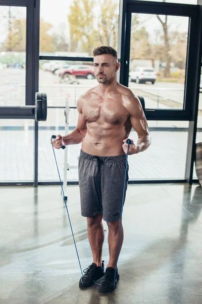 handsome shirtless sportsman training with jumping rope in gym