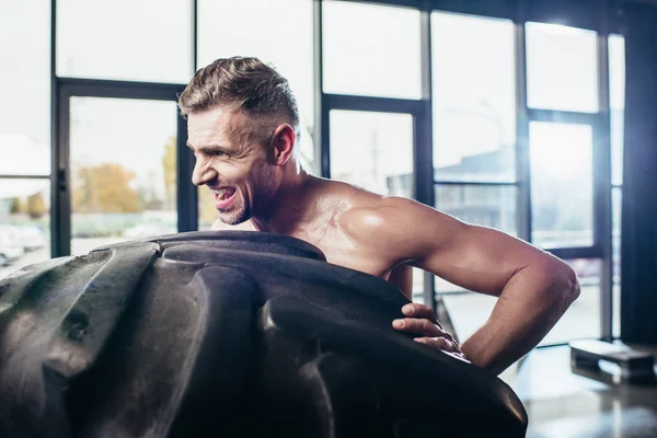 Seitenansicht Eines Gutaussehenden Hemdlosen Sportlers Der Reifen Hebt Und Grimassen — kostenloses Stockfoto