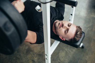 yakışıklı sporcu spor salonunda bankta yalan sırasında halter ağırlık kaldırma, yüksek açılı görünüş 