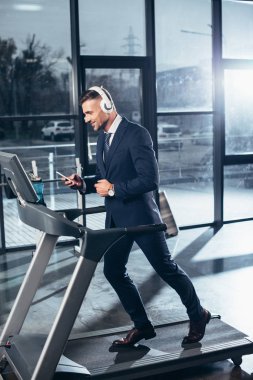 koşu bandında egzersiz ve spor salonunda smartphone ile müzik dinleme elbiseli yakışıklı işadamı yan görünüm