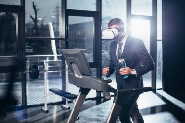 işadamı takım elbise ve treadmill egzersiz ve spor salonunda spor şişe tutan bir sanal gerçeklik kulaklık