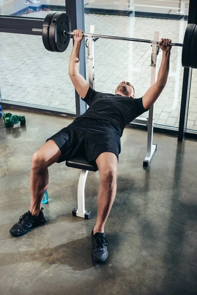 英俊的运动员举起杠铃与重量 而躺在长凳上在健身房 — 图库照片