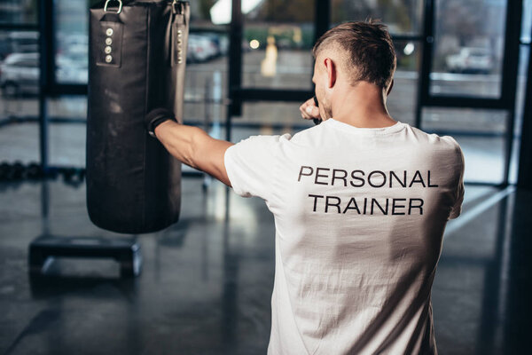 back view of personal trainer boxing with punching bag in gym