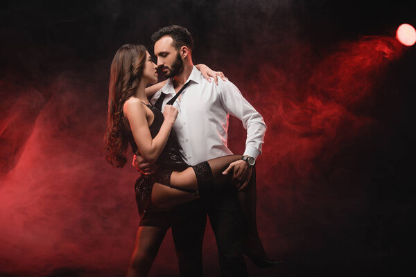 heterosexual passionate couple hugging in red smoky room 