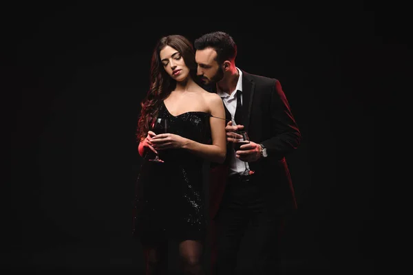 性感的夫妇在黑色礼服和燕尾服持有眼镜与红葡萄酒隔离在黑色 — 图库照片