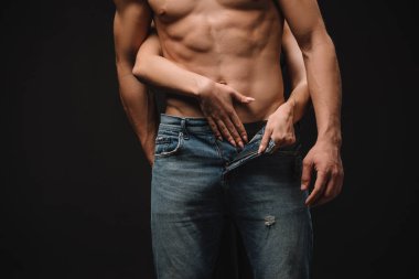 cropped view of passionate woman undressing shirtless man in jeans isolated on black clipart