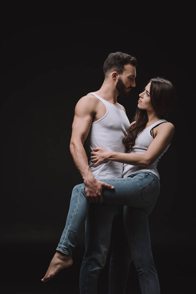 handsome man hugging woman in white singlet and jeans isolated on black