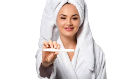 çekici kız gülümseyerek, hamilelik testi gösterilen ve üzerinde beyaz izole kamera bakarak bornoz