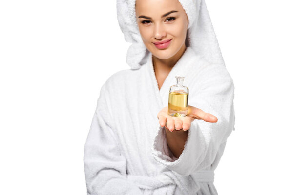 привлекательная девушка в халате с бутылкой масла и смотрящая на камеру, изолированную на белом
