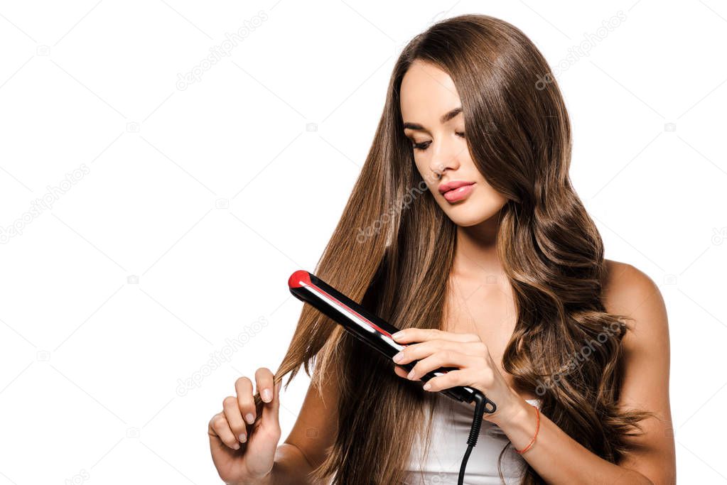 attractive girl holding hair and using straightener isolated on white