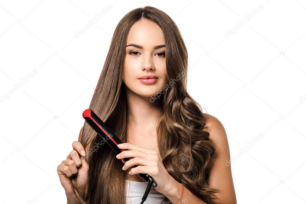 beautiful girl with long brown hair using straightener and looking at camera isolated on white