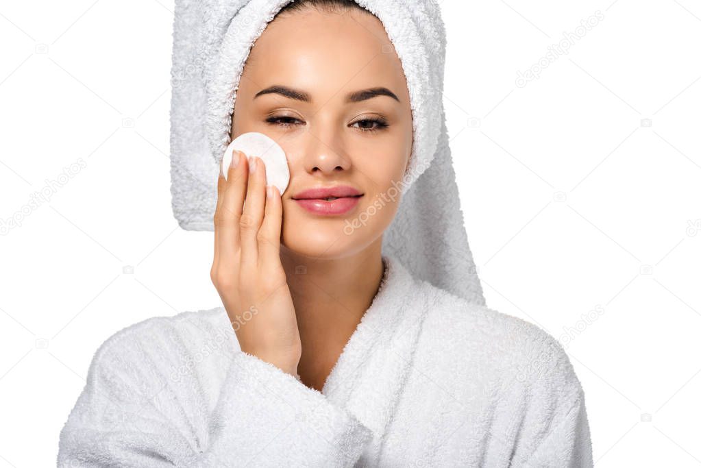 close up view of attractive girl in bathrobe cleaning face with cotton sponge and looking at camera isolated on white