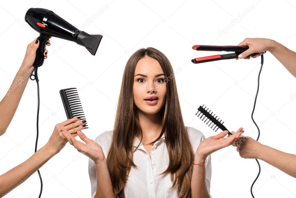 women holding accessories of hairdresser around surprised girl gesturing with hands isolated on white