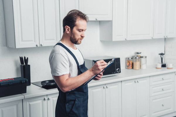 adult repairman in working writing in clipboard in kitchen at home