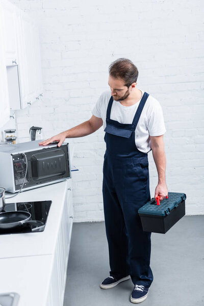 high angle view of adult handyman with toolbox checking microwave oven in kitchen