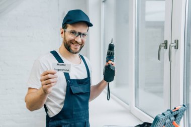 elektrikli matkap tutan ve kart ev muayene yazı ile gösterilen mutlu yetişkin erkek ustası