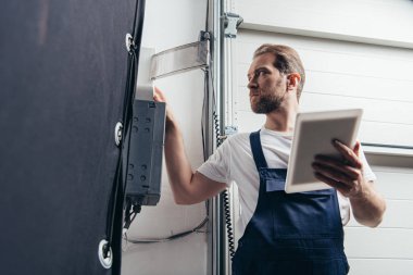 Erkek sakallı tamircisi elektrik kutusunu kontrol dijital tablet ile düşük açılı görünümü 