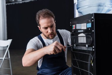 bearded male craftsman repairing water cooler with screwdriver  clipart