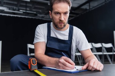 serious male handyman making measurements and writing in clipboard clipart