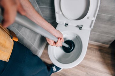 cropped shot of male plumber using plunger and cleaning toilet in bathroom  clipart