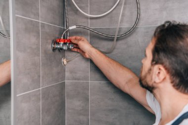 selective focus of male plumber repairing electric boiler in bathroom  clipart