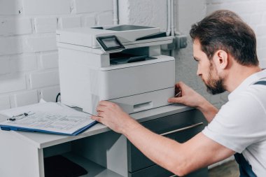 focused male handyman repairing copy machine in modern office  clipart
