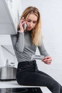 ev muayene yazı ve mutfakta Smartphone cep telefonu ile konuşurken ile kart tutan güzel genç kadın 