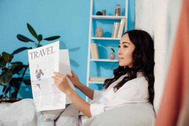 güzel gülümseyen Asyalı kız yatakta seyahat gazete okuma yan görünüm