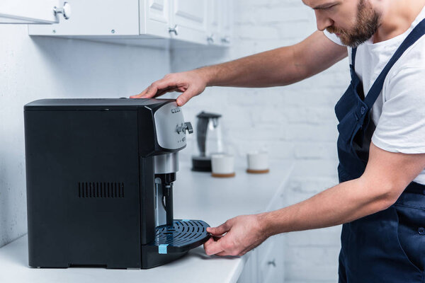partial view of handyman in working overall repairing coffee machine in kitchen