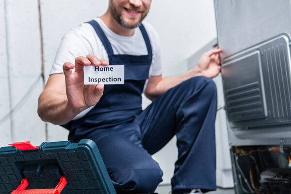 partial view of adult craftsman showing card with lettering home inspection while sitting near broken refrigerator 