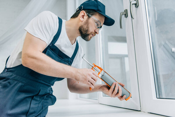 bearded adult repairman fixing window with sealant gun