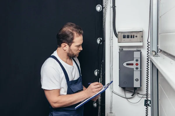 Mężczyzna Elektryk Pisania Schowku Sprawdzanie Skrzynki Elektrycznej — Zdjęcie stockowe