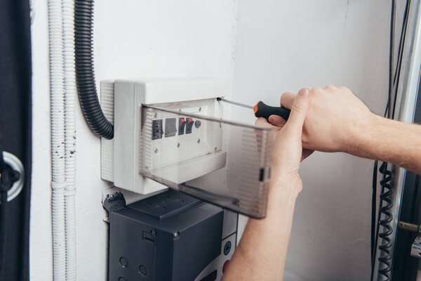 cropped image of male electrician repairing electrical box by screwdriver 