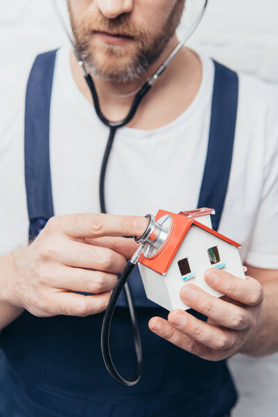 частичный взгляд бородатого ремонтника, проверяющего фигуру дома по стетоскопу, концепция домашней инспекции
