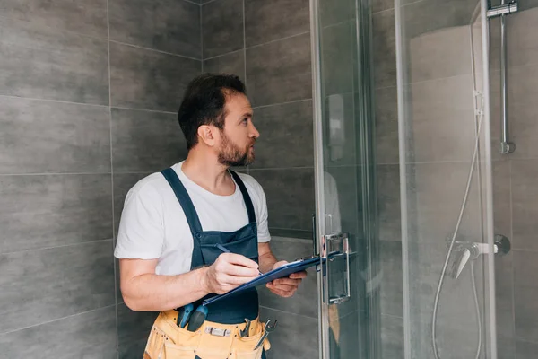 成年男性水管工在剪贴板做笔记 同时检查淋浴在浴室 — 图库照片