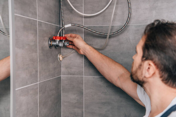 selective focus of male plumber repairing electric boiler in bathroom 