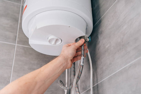 cropped shot of male plumber repairing electric boiler in bathroom 