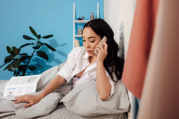 Bela Jovem Segurando Jornal Falando Por Smartphone Cama — Fotografia de Stock